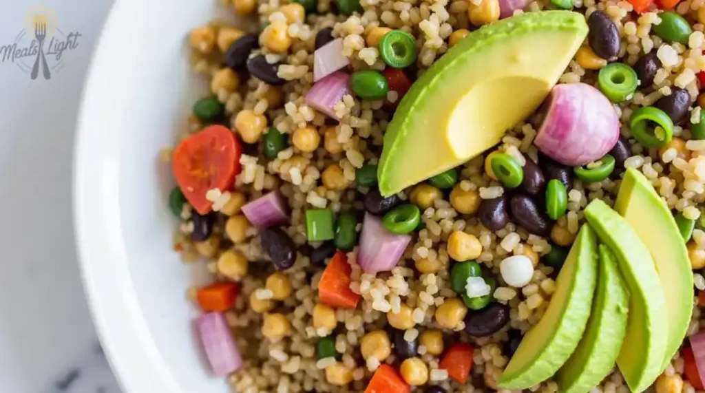  A colorful grain bowl topped with avocado slices, black beans, chickpeas, red onion, cherry tomatoes, green peas, and red bell peppers.